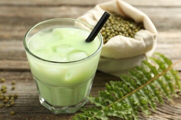 Fresh mung bean juice with ice in glass, leaves and seeds on wooden table, closeup