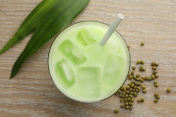 Fresh mung bean juice with ice in glass, leaves and seeds on wooden table, flat lay