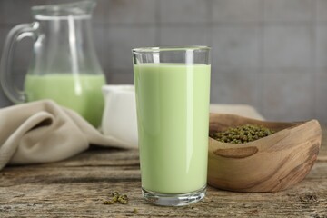 Fresh mung bean juice in glass and seeds on wooden table against grey tiled wall, closeup