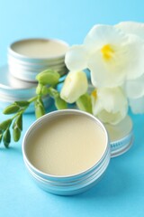 Lip balms and freesia flowers on light blue background, closeup