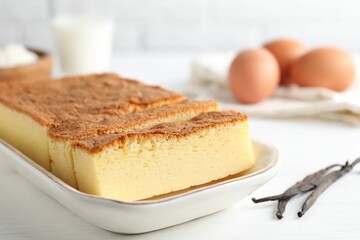 Tasty Japanese Castella sponge cake and ingredients on white table, closeup