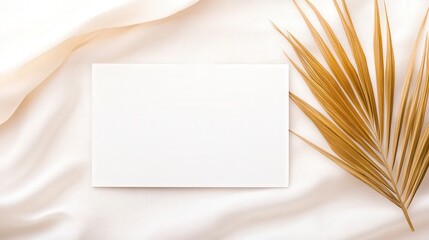 A blank rectangular card lies on soft fabric alongside a dried golden leaf, creating a serene and minimalistic aesthetic.