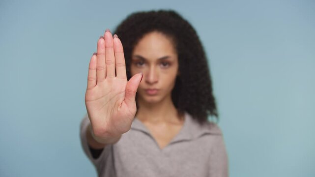 Serious woman making stop hand gesture on blue background