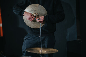 Close-up image of a musician adjusting the setup of a cymbal on a drum set, likely in preparation for a performance or recording in a music studio. Captures focus and dedication to the craft.