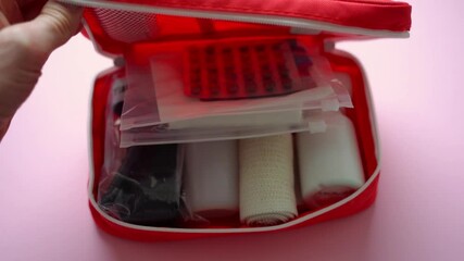 A hand stretches out to grasp a bright red first aid kit, undeniably symbolizing the vital importance of preparedness and safety during emergencies, whether at home or while traveling