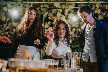 Friends gather in an outdoor setting, engaging in a lively beer pong game during a birthday celebration, surrounded by illuminated decorations and a cheerful atmosphere.