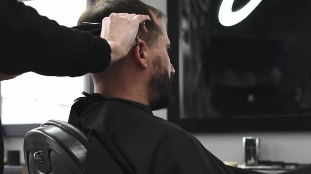 Skilled barber trimming client's hair using professional scissors, creating precise hairstyle in contemporary salon with modern interior and relaxed atmosphere.