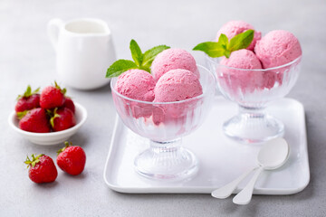 Ice cream with strawberry in a glass bowl on white plate. Grey background. Close up.
