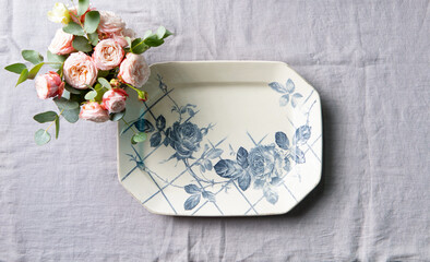 Roses flowers bunch and vintage plate on a table. Grey textile background. Top view.