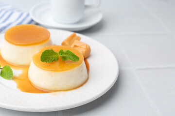Tasty puddings with caramel sauce served on white tiled table, closeup. Space for text