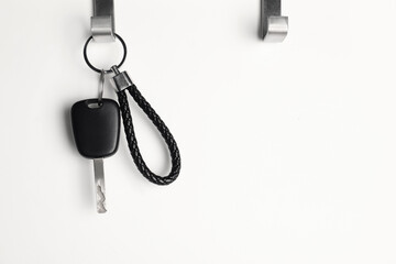 Car key hanging on light wall, space for text