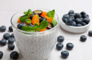 Delicious chia pudding with blueberries, peaches and mint in glass on white table, closeup