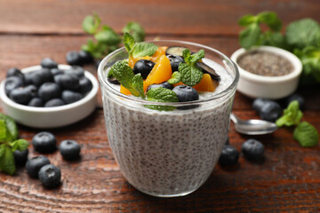 Delicious chia pudding with blueberries, peaches and mint in glass on wooden table, closeup