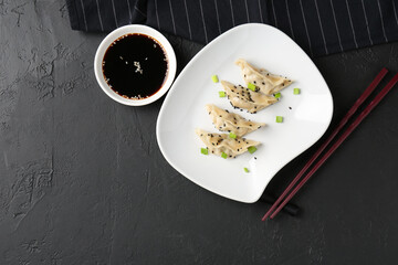 Delicious gyoza dumplings with chives and sesame seeds served on black table, top view. Space for text