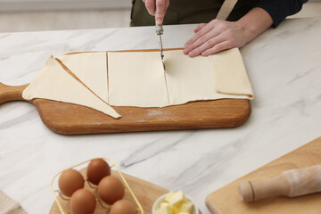 Woman cutting dough at light marble table, closeup. Making croissants