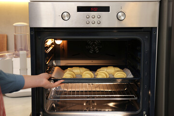 Woman putting baking sheet with raw croissants into oven indoors, closeup