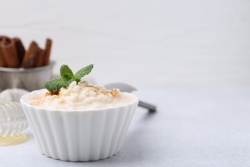 Tasty rice pudding with cinnamon and mint on light grey table, closeup. Space for text