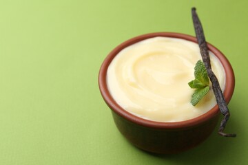 Tasty vanilla pudding, mint and pod on green background, closeup. Space for text