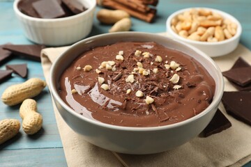 Tasty chocolate pudding in bowl and ingredients on light blue wooden table, closeup