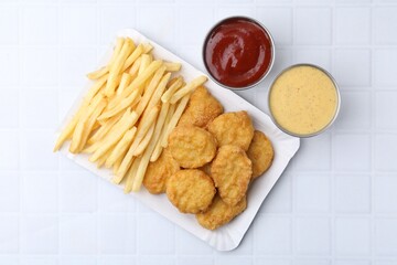 Tasty chicken nuggets and french fries with sauce on white tiled table, top view