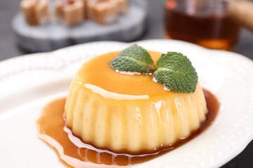 Delicious pudding with caramel sauce and mint on table, closeup