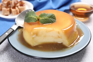 Delicious pudding with caramel sauce, mint and spoon on grey textured table, closeup