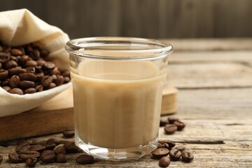 Coffee cream liqueur in glass and beans on wooden table, closeup