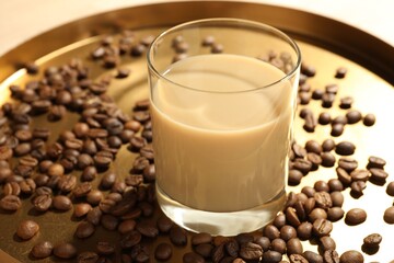 Coffee cream liqueur in glass and beans on tray, closeup