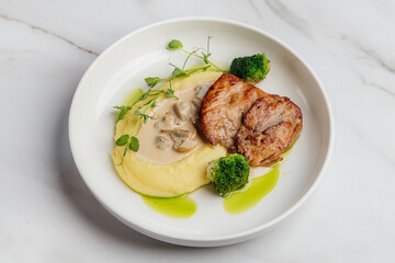Grilled chicken breast is served with creamy mashed potatoes, steamed broccoli florets, fresh pea shoots, and a rich mushroom sauce. Restaurant or cafe menu, cookbook recipe