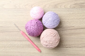 Balls of colorful yarn and crochet hook on wooden table, flat lay
