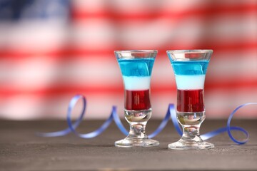 Tasty cocktails in shot glasses and serpentine streamer on grey table against flag of USA, space for text
