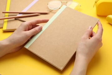 Woman with different copybooks and other stationery on yellow background, closeup