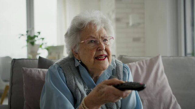 Adorable old woman watching television, holding TV remote controller.
