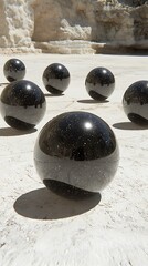 Several glossy black spheres rest on a textured white surface outdoors