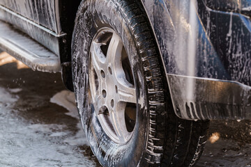 Close-up Image of a Car Wheel Covered with Soap Foam During a Vehicle Wash