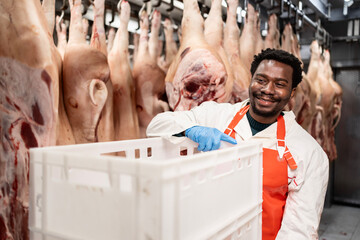 Experienced butcher holding basket full of chopped meat in slaughterhouse.