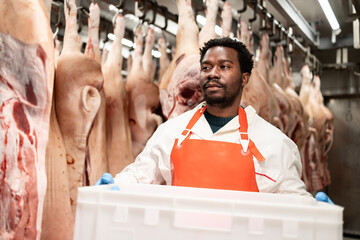 Experienced butcher holding basket full of chopped meat in slaughterhouse.