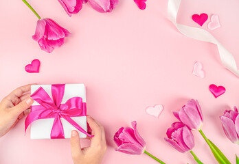 Gift box in hands with flowers tulips on pink background. happy mothers day, top view. copy space