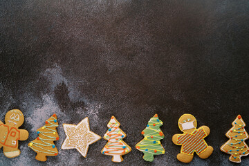 Colorful Christmas glazed cookies lie along the bottom edge on a black shabby background