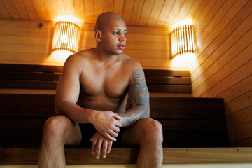 Tattooed african american man sitting in sauna in spa complex
