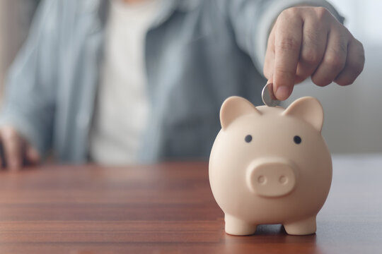 Man putting coins in piggy bank and taking notes in notebook money saving concept business