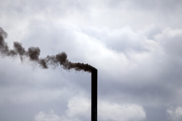 
a black column of smoke rising from a pipe against a cloudy sky.