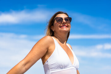 Portrait of beautiful happy middle aged woman standing against background of blue sky in summertime	