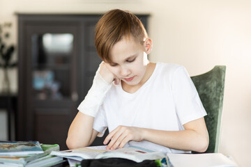 Naklejka premium Kid teenager boy pupil at home making homework with broken finger. Child hand with a cast.