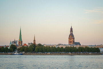 Fototapeta premium View of Riga Old Town with green trees and Daugava river on the bottom on soft sunset gradient sky background