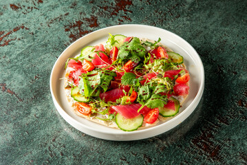 A vibrant plate featuring fresh sushi with sliced cucumbers, cherry tomatoes, and garnished with cilantro, beautifully presented on a textured green background.
