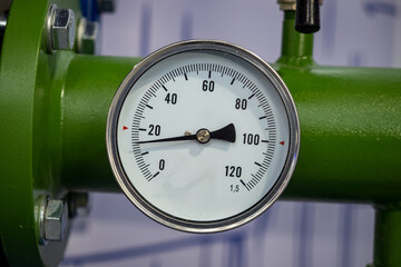 A round pressure gauge with a white dial and black markings is mounted on a green industrial pipe,...