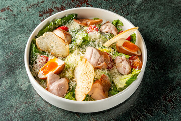 A vibrant salad bowl filled with fresh lettuce, chunks of tender chicken, cherry tomatoes, creamy dressing, and crispy toppings, set against a textured green background.