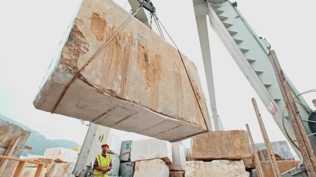 Raw marble block transportation in a stone processing facility. A large stone block is lifted by a crane and brought into the factory for processing.
