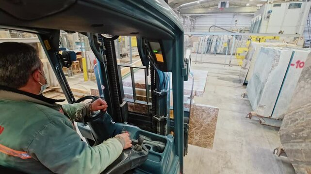 Forklift operator transporting stone slabs in a marble factory. A worker uses a forklift to safely move large stone panels.